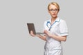 Beautiful Caucasian woman doctor or nurse holding a laptop pc computer standing over grey background Royalty Free Stock Photo