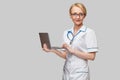 Beautiful Caucasian woman doctor or nurse holding a laptop pc computer standing over grey background Royalty Free Stock Photo