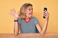 Beautiful caucasian woman doing video call waving to smartphone sticking tongue out happy with funny expression