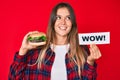 Beautiful caucasian woman eating a tasty classic burger holding wow text smiling looking to the side and staring away thinking Royalty Free Stock Photo