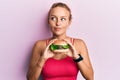 Beautiful caucasian woman eating a tasty classic burger smiling looking to the side and staring away thinking Royalty Free Stock Photo