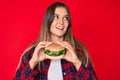 Beautiful caucasian woman eating a tasty classic burger smiling looking to the side and staring away thinking Royalty Free Stock Photo