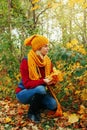 Beautiful Caucasian woman girl wearing yellow knitted scarf and hat sitting in autumn fall park forest Royalty Free Stock Photo