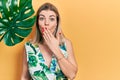 Beautiful caucasian woman with green plant leaf close to beautiful face covering mouth with hand, shocked and afraid for mistake Royalty Free Stock Photo