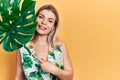 Beautiful caucasian woman with green plant leaf close to beautiful face smiling happy pointing with hand and finger Royalty Free Stock Photo