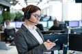 Beautiful caucasian woman in headset is holding a mobile phone while standing in open space office. Friendly female Royalty Free Stock Photo
