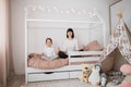 Beautiful caucasian woman and her cute little preschooler daughter sitting on wooden childs bed