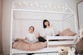 Beautiful caucasian woman and her cute little preschooler daughter sitting on wooden childs bed