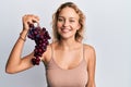 Beautiful caucasian woman holding branch of fresh grapes looking positive and happy standing and smiling with a confident smile Royalty Free Stock Photo