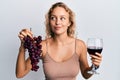 Beautiful caucasian woman holding branch of fresh grapes and red wine smiling looking to the side and staring away thinking Royalty Free Stock Photo