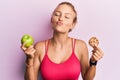 Beautiful caucasian woman holding green apple and cookie looking at the camera blowing a kiss being lovely and sexy Royalty Free Stock Photo