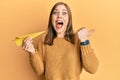 Beautiful caucasian woman holding paper airplane pointing thumb up to the side smiling happy with open mouth Royalty Free Stock Photo