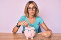 Beautiful caucasian woman holding piggy bank with glasses relaxed with serious expression on face Royalty Free Stock Photo