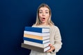 Beautiful caucasian woman holding a pile of books afraid and shocked with surprise and amazed expression, fear and excited face Royalty Free Stock Photo