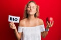 Beautiful caucasian woman holding red apple and bio word looking at the camera blowing a kiss being lovely and sexy Royalty Free Stock Photo