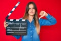 Beautiful caucasian woman holding video film clapboard with angry face, negative sign showing dislike with thumbs down, rejection