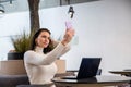 beautiful caucasian woman makes selfie on a smartphone sitting at a table with a laptop. a blogger creates content, a