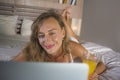 Beautiful Caucasian woman 30s lying on bed at night in home bedroom using internet at laptop computer drinking healthy orange juic Royalty Free Stock Photo