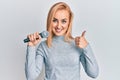Beautiful caucasian woman singing song using microphone smiling happy and positive, thumb up doing excellent and approval sign Royalty Free Stock Photo