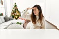 Beautiful caucasian woman sitting on the table by christmas tree very happy and smiling looking far away with hand over head Royalty Free Stock Photo