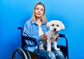 Beautiful caucasian woman sitting on wheelchair hugging dog thinking attitude and sober expression looking self confident Royalty Free Stock Photo