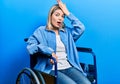 Beautiful caucasian woman sitting on wheelchair surprised with hand on head for mistake, remember error