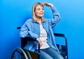 Beautiful caucasian woman sitting on wheelchair very happy and smiling looking far away with hand over head Royalty Free Stock Photo