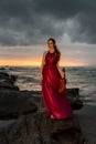 Beautiful Caucasian woman with violin on the beach. Music and art concept. Slim girl wearing long red dress and holding violin in Royalty Free Stock Photo