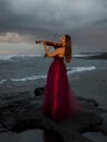 Beautiful Caucasian woman with violin on the beach. Music and art concept. Slim girl wearing long red dress and playing violin in Royalty Free Stock Photo