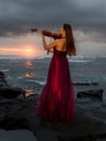 Beautiful Caucasian woman with violin on the beach. Music and art concept. Slim girl wearing long red dress and playing violin in Royalty Free Stock Photo