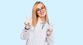 Beautiful caucasian woman wearing doctor uniform and stethoscope smiling looking to the camera showing fingers doing victory sign Royalty Free Stock Photo