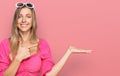 Beautiful caucasian woman wearing sunglasses and summer style amazed and smiling to the camera while presenting with hand and Royalty Free Stock Photo