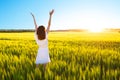 Beautiful caucasian woman in white dress jumping up with raised hands outdoor. Field with yellow wheat around