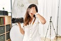 Beautiful caucasian woman working as photographer at photography studio covering eyes with hand, looking serious and sad