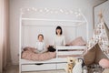 Beautiful caucasian woman and her cute little preschooler daughter sitting on wooden childs bed