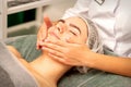 Beautiful caucasian young woman receiving a facial massage with closed eyes in spa salon, close up. Relaxing treatment Royalty Free Stock Photo