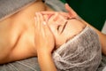 Beautiful caucasian young woman receiving a facial massage with closed eyes in spa salon, close up. Relaxing treatment Royalty Free Stock Photo