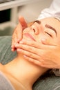 Beautiful caucasian young woman receiving a facial massage with closed eyes in spa salon, close up. Relaxing treatment Royalty Free Stock Photo