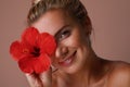 Beautiful caucasian young woman with red flower. Stunning blonde girl with big flower posing over beige background. Royalty Free Stock Photo