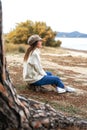 Beautiful Caucasian young woman sitting near the water on a tree trunk in pine forest enjoying the magic winter sea. Happy female