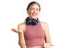 Beautiful caucasian young woman wearing gym clothes and using headphones smiling cheerful with open arms as friendly welcome, Royalty Free Stock Photo