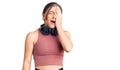 Beautiful caucasian young woman wearing gym clothes and using headphones yawning tired covering half face, eye and mouth with hand Royalty Free Stock Photo