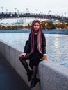 Beautiful Caucasse woman with long pink dreadlocks and pigtails in black clothes sits on the parapet of the Moscow River Royalty Free Stock Photo