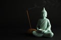 Beautiful ceramic Buddha sculpture with burning candle and incense stick on black background. Space for text Royalty Free Stock Photo