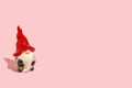 Beautiful ceramic Christmas gnome with red hat on pink background. Winter holiday concept. Pink Christmas