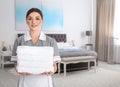 Chambermaid with clean folded towels near bed in hotel room