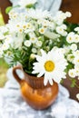 Beautiful chamomile flowers on a wooden old chair along with a lace doily on a green garden background. Summer atmosphere, simple