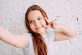 Beautiful charming redhead smiling teenager girl taking selfie on frontal camera isolated on white brick wall Royalty Free Stock Photo