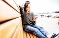 Beautiful charming young funny happy girl with curly hair and a smartphone in her hands sits on a bench in the city Royalty Free Stock Photo