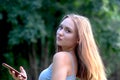 Beautiful charming young girl with long hair stands against the background of nature on a sunny day,